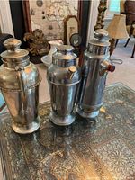 Photo showing the three stainless steel carafes placed side by side on decorative table surface, highlighting their varying shapes and patina.