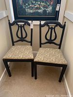Pair of black wooden harp back chairs with tan paisley upholstered seats positioned side by side in a hallway.