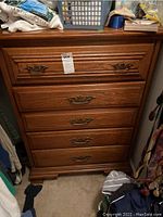 Frontal view showing the wooden chest with five drawers, dark brass handles, and carved wood detailing.