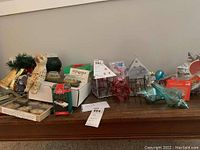 Photo of assorted Christmas decorations including ceramic cat figurine, Christmas bells, ceramic houses, hallmark ornament box, glass ornaments, and candle holder lanterns.
