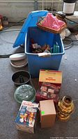 Photo showing blue plastic tote open with visible items including linens in wicker basket, cooler, pie cooler box, Sunbeam fondue box, and various small kitchen items