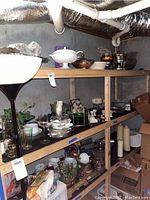 Shelves stocked with various glass plates, metal and glass serving bowls, glassware, and some candles.