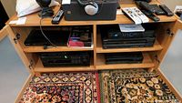 Wide view of shelving unit with Yamaha tuner, Sony Blu-ray player, stereo receiver, remotes and headphones on top shelf, cords visible on shelves below