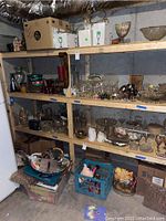 Shelves of assorted glassware and serving pieces, two-tier wooden shelving in basement. Items include glass bowls, glasses, pitchers, and some ceramics.