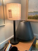 Black buffet style lamp on table with beige fabric shade lit, black conical lampshade with gold interior beside it