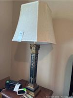 Full view of one lamp showing beige canvas shade, black base with gold detailing, and cord at the base.