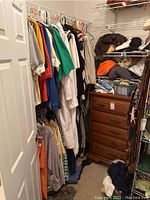 Wide view of closet showing hanging shirts, shelving with folded clothes, wooden dresser, belts.