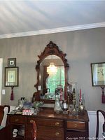Full view of ornate wooden carved mirror mounted above a wooden sideboard, showing reflective glass and decorative woodwork.