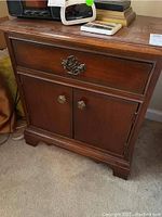 Front view of a wooden nightstand with one drawer and cabinet doors below, showing metal drawer pull and knobs.