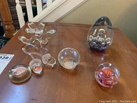 Overview of six glass and crystal decorative items including paperweights and crystal acorns arranged on wooden surface.