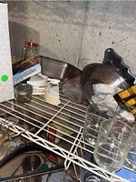 Shelf with various kitchen items including glassware, metal pans, utensils, boxed chicken roaster