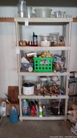 Full view of the shelving unit filled with various household and garage items including containers, green plastic crate, jars, and cleaning supplies.