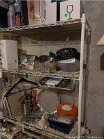 White wire shelving unit loaded with assorted kitchen items including glassware, bowls, baking pans, and containers.