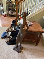 Photo showing the full height and stance of the metal female statue placed on carpet near a wooden side table and stair railing.
