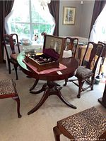 Dining table shown in a room setting with several chairs around it, highlighting table's cherry finish and claw feet base.