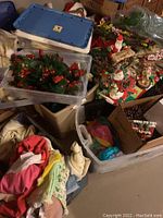 Photo showing vintage blue camp trunk with brass accents, assorted towels, and Christmas decorations stacked in plastic bins and cardboard boxes.