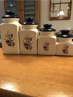 Photo of four ceramic canisters in descending size order featuring floral designs and black lids