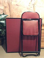 Photo showing the folded card table and one folding chair, highlighting the red surfaces and black metal framework.