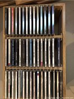 Top-down view of wooden CD case filled with rows of standard-sized music CDs.
