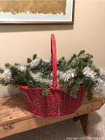 Red basket with green pine garland and white tinsel from front view