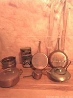 Copper cookware items and two vintage Canada Straight tins arranged on a table against a beige backdrop.