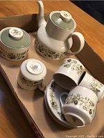 Photo showing coffee pot, sugar bowl with lid, cream pitcher, and several cups with saucers featuring green and brown floral pattern.