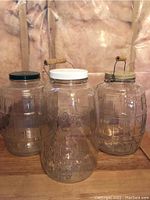 Photo showing three clear glass jars with lids and handles, highlighting central embossed jar with ''MASON'' lettering and rooster design