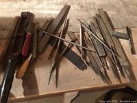 Assorted metal and wood files spread out on a wooden surface, various sizes and types including flat, round, and rasp files.