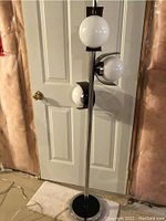 Full view of retro floor lamp showing three white globe shades on a chrome and black base.