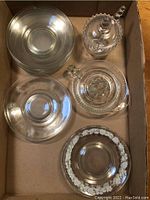 Overhead view of glass plates, lemon squeezer, and jam jar with spoon in cardboard box.