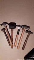 Photo showing six various hammers including claw hammers, small sledgehammer, and ball peen hammers with wooden handles and metal heads.