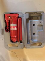 Red 6 ton hydraulic bottle jack with two removable red metal pump handles, all housed in a molded grey plastic carrying case.