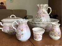 Seven-piece pink floral jug and basin set displayed on wooden table.