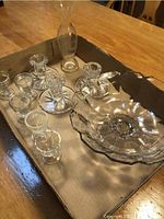 Photo of the lot showing a large glass bowl, six glass egg cups, one slender glass vase, and three glass candle holders arranged in a tray on a wooden table.