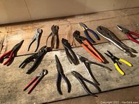 Photo showing 14 assorted pliers on a wooden surface with varied handle colors and jaw types.
