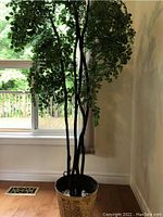 Artificial tree with green leaves, dark brown multiple trunks, in decorative pot placed near window with natural light