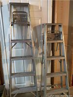 Front view of two step ladders side by side, showing 6-step and 5-step aluminum ladders with tool trays at the top.