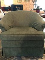 Front view of one green upholstered armchair with rounded back, cushioned seat, and fabric skirt, showing ribbed texture and some wear.