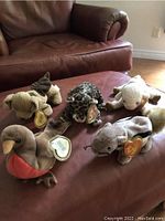 Image showing six different Ty Beanie Babies arranged on a leather ottoman: kangaroo, leopard, lamb, bird, squirrel and another.