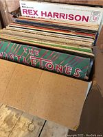Box of vinyl records showing spines of multiple LPs including Rex Harrison and The Mistletones with some covers appearing water stained
