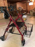 Side view of the red walker showing padded seat, front basket, and foldable frame in a basement setting.