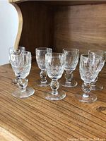 Photo of eight Waterford liqueur glasses arranged in two rows on a wooden surface highlighting their short stems and intricate cut pattern.