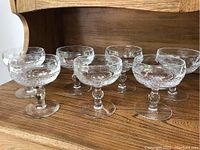 Seven clear crystal Waterford sherbet glasses with diamond cut pattern, short stems, arranged on a wooden surface.