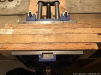 Woodworking vise mounted on wood bench with steel screw and guide rods visible