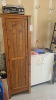 Tall wood cabinet closed, showing vertical slatted wood finish door with knob