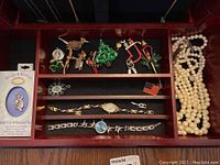 Photo of one jewelry tray with brooches, watches, and a white beaded necklace