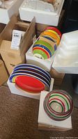 Multiple colorful striped plates arranged in foam packaging with cardboard boxes around
