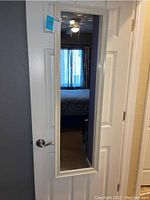 Front view of the full-length wood framed mirror hanging over a white door, reflecting part of a bedroom.