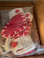 Two red and white knitted stocking cutlery holders in packaging, designed to hold cutlery in a holiday style.