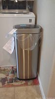 Full view of stainless steel kitchen waste can with plastic liner inside and manual attached.